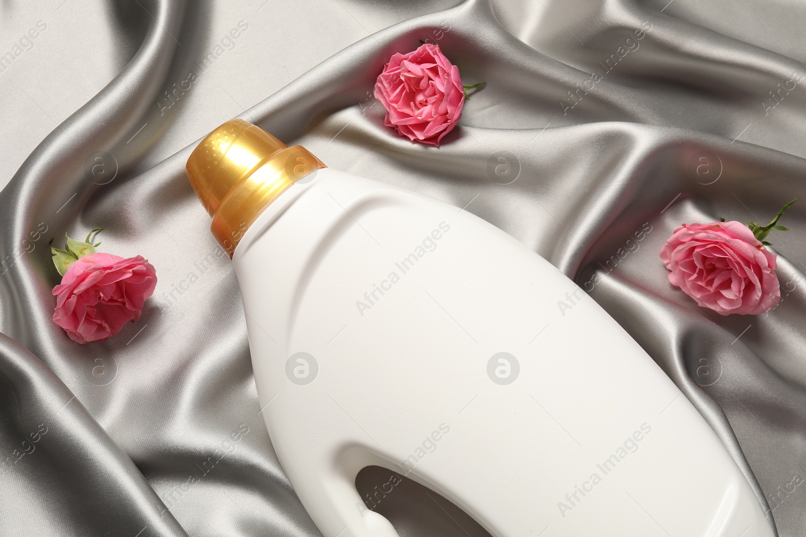 Bottle of fabric softener and flowers on grey cloth, flat lay Photo of Bottle of fabric softener and flowers on grey cloth, flat lay