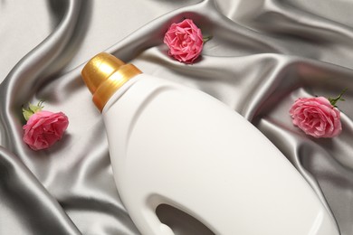 Photo of Bottle of fabric softener and flowers on grey cloth, flat lay
