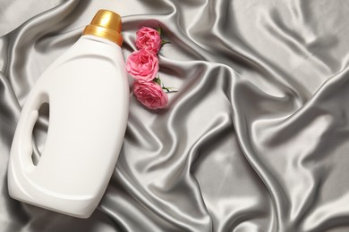 Photo of Bottle of fabric softener and flowers on grey cloth, flat lay. Space for text
