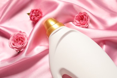 Photo of Bottle of fabric softener and flowers on pink cloth, above view