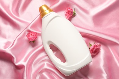 Photo of Bottle of fabric softener and flowers on pink cloth, flat lay