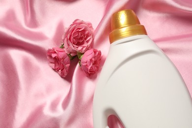 Photo of Bottle of fabric softener and flowers on pink cloth, flat lay