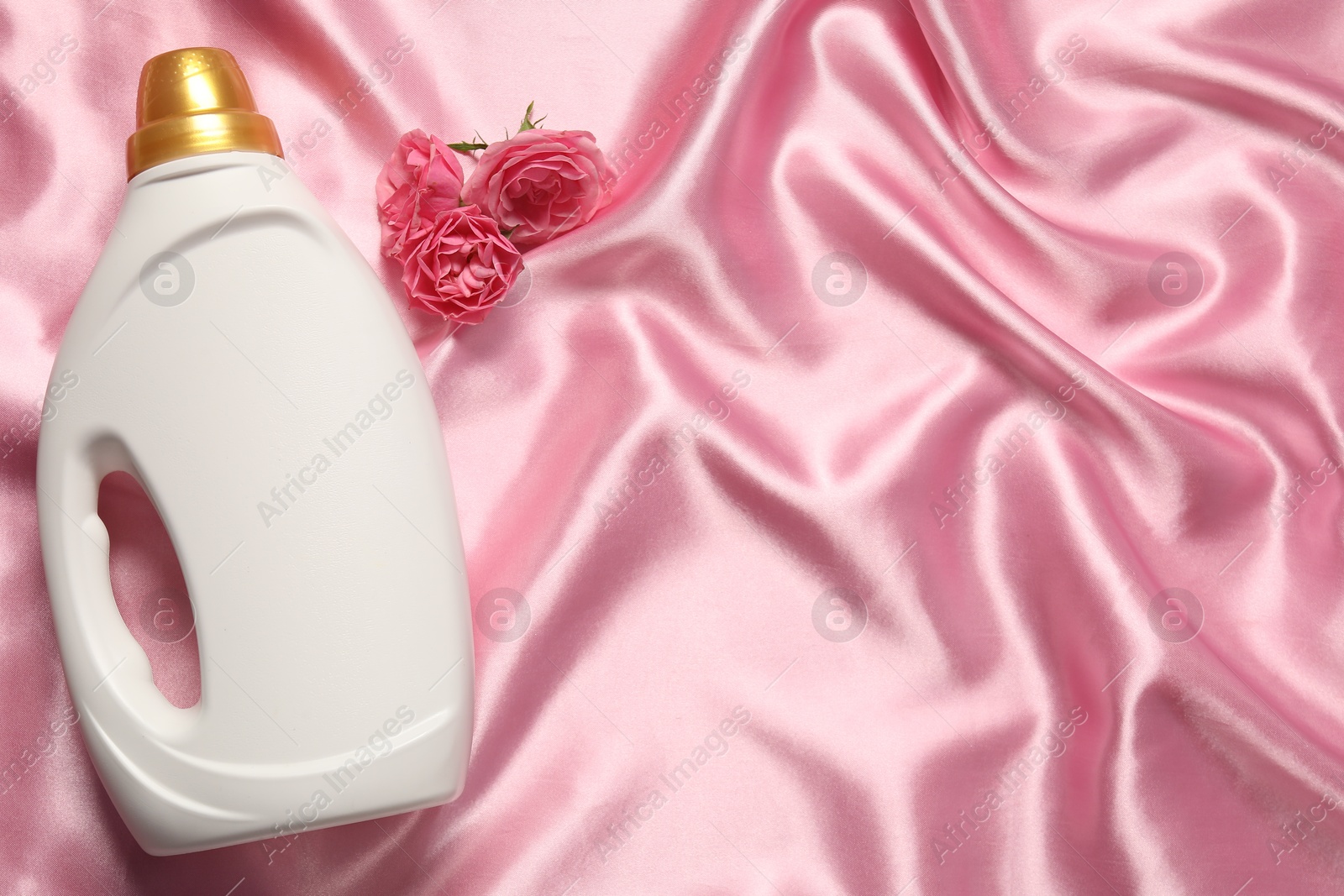 Photo of Bottle of fabric softener and flowers on pink cloth, flat lay. Space for text