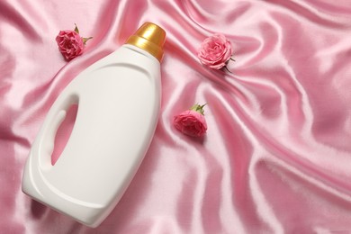 Photo of Bottle of fabric softener and flowers on pink cloth, flat lay. Space for text