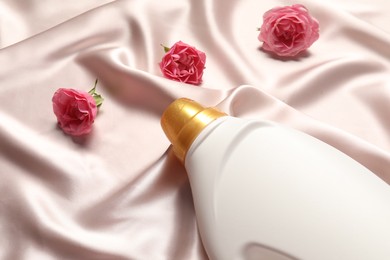 Photo of Bottle of fabric softener and flowers on beige cloth, above view