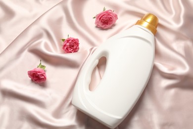 Photo of Bottle of fabric softener and flowers on beige cloth, flat lay