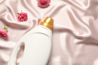 Photo of Bottle of fabric softener and flowers on beige cloth, flat lay. Space for text