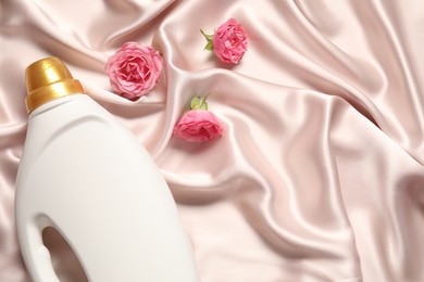 Photo of Bottle of fabric softener and flowers on beige cloth, flat lay. Space for text