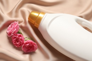 Photo of Bottle of fabric softener and flowers on beige cloth, above view