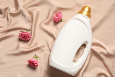Photo of Bottle of fabric softener and flowers on beige cloth, flat lay