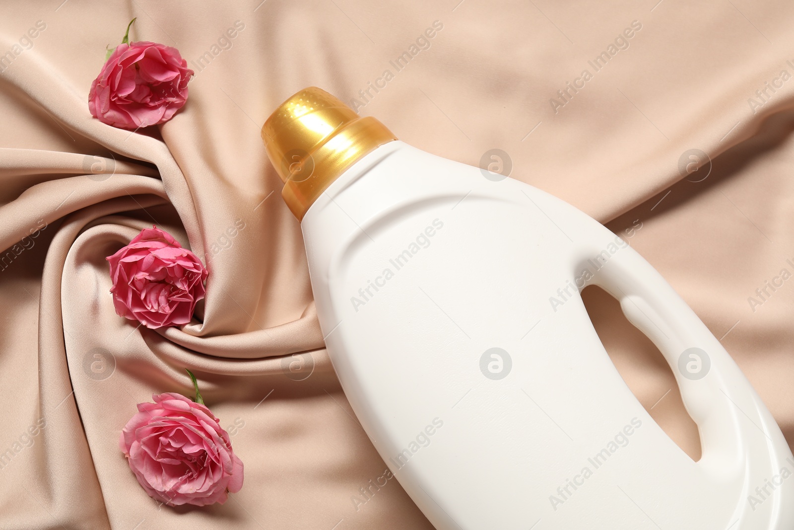 Bottle of fabric softener and flowers on beige cloth, flat lay Photo of Bottle of fabric softener and flowers on beige cloth, flat lay