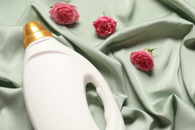 Photo of Bottle of fabric softener and flowers on green cloth, above view