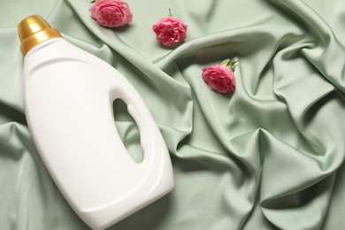 Photo of Bottle of fabric softener and flowers on green cloth, flat lay. Space for text