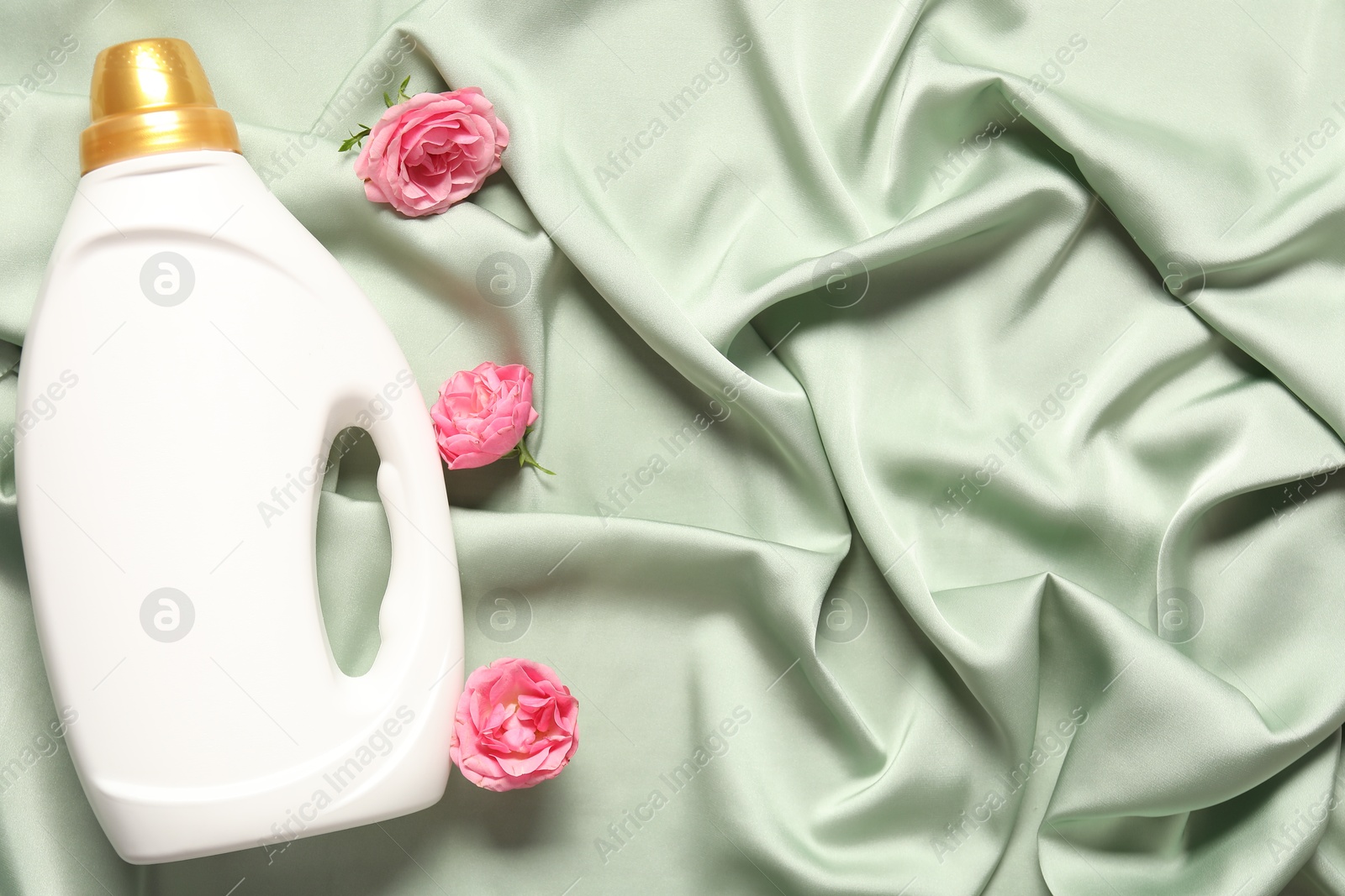 Photo of Bottle of fabric softener and flowers on green cloth, flat lay. Space for text
