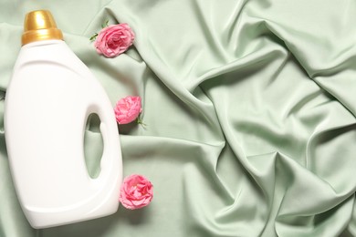 Photo of Bottle of fabric softener and flowers on green cloth, flat lay. Space for text