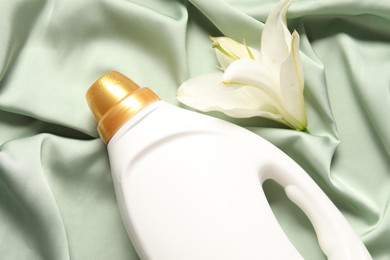Photo of Bottle of fabric softener and flower on green cloth, above view