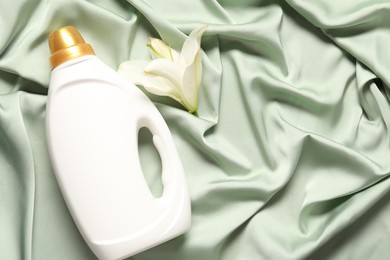 Photo of Bottle of fabric softener and flower on green cloth, flat lay. Space for text