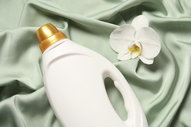 Photo of Bottle of fabric softener and orchid flower on green cloth, flat lay