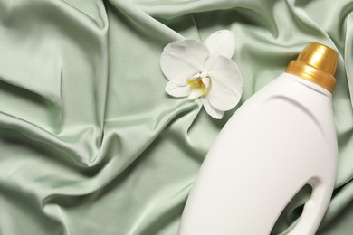 Photo of Bottle of fabric softener and orchid flower on green cloth, flat lay. Space for text
