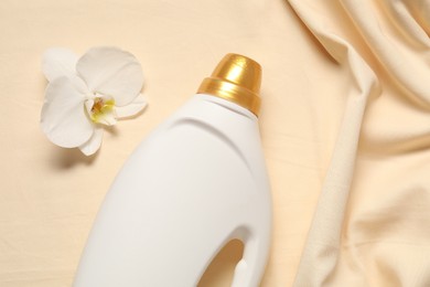 Photo of Bottle of fabric softener and orchid flower on beige background, flat lay