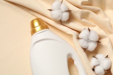 Photo of Bottle of fabric softener and cotton flowers on beige background, flat lay