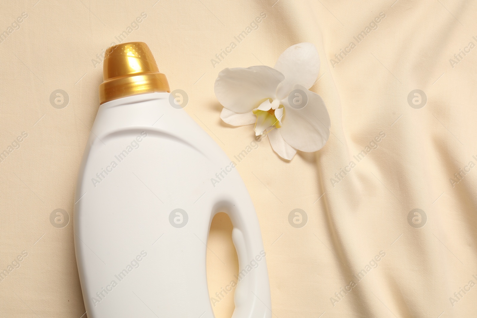 Photo of Bottle of fabric softener and orchid flower on beige background, flat lay