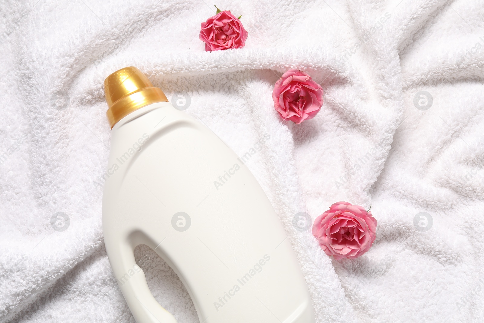 Photo of Bottle of fabric softener and flowers on terry towel, flat lay