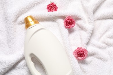 Photo of Bottle of fabric softener and flowers on terry towel, flat lay