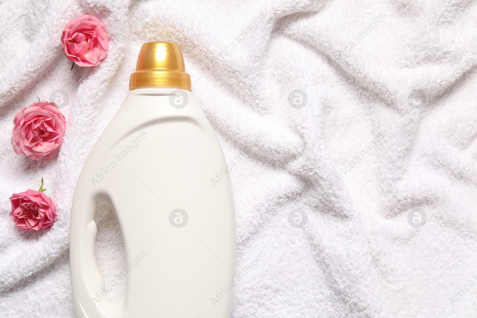 Photo of Bottle of fabric softener and flowers on terry towel, flat lay. Space for text