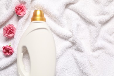 Photo of Bottle of fabric softener and flowers on terry towel, flat lay. Space for text