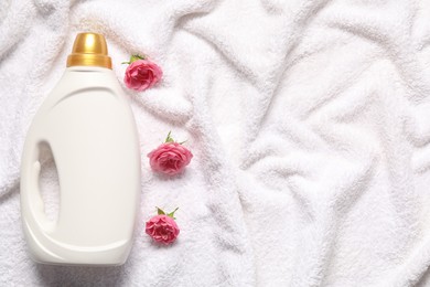 Photo of Bottle of fabric softener and flowers on terry towel, flat lay. Space for text