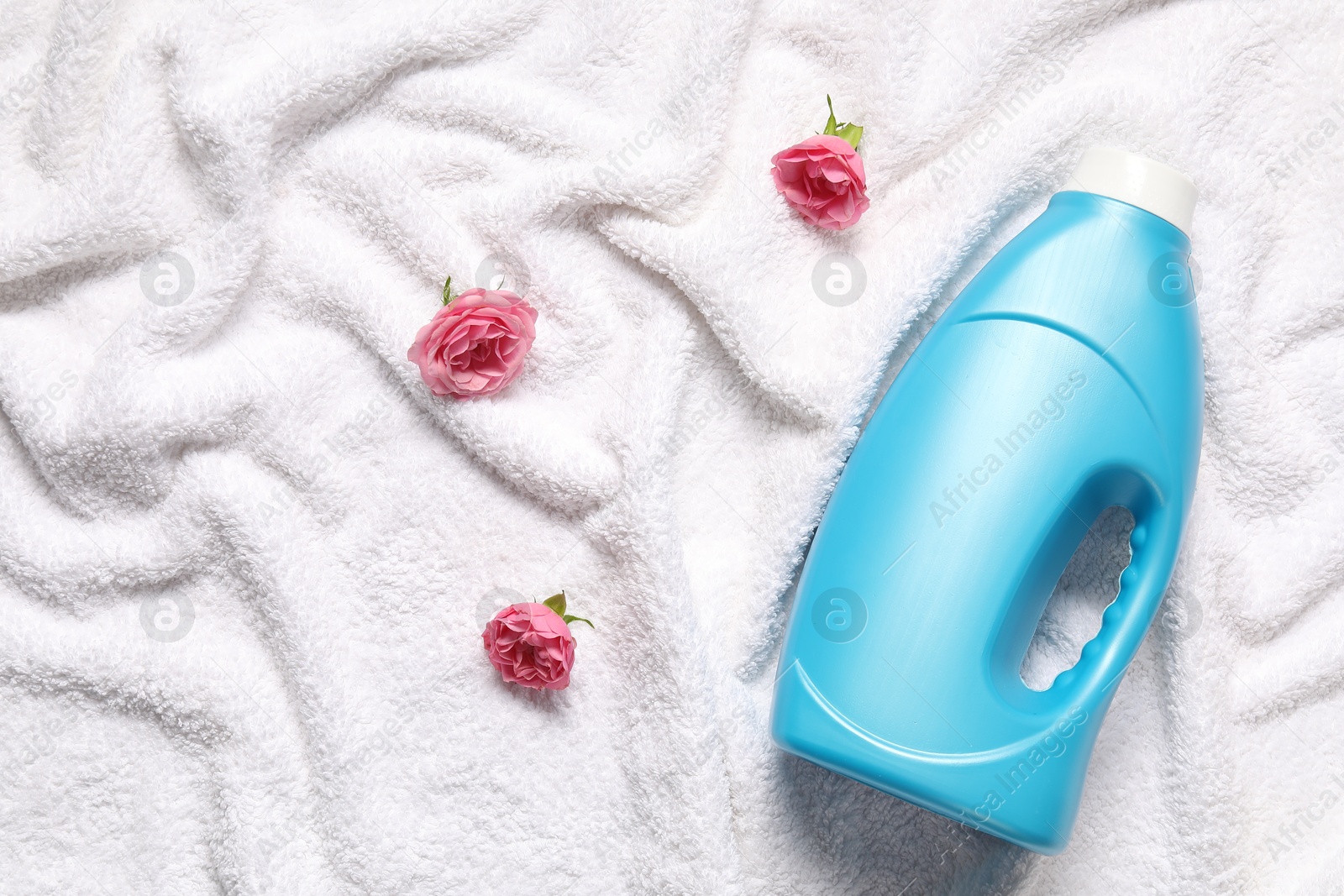 Bottle of fabric softener and flowers on terry towel, flat lay Photo of Bottle of fabric softener and flowers on terry towel, flat lay