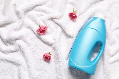 Photo of Bottle of fabric softener and flowers on terry towel, flat lay
