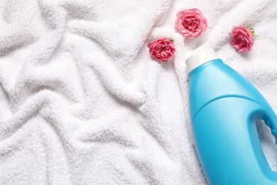Photo of Bottle of fabric softener and flowers on terry towel, flat lay. Space for text