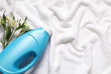 Photo of Bottle of fabric softener and flowers on terry towel, flat lay. Space for text