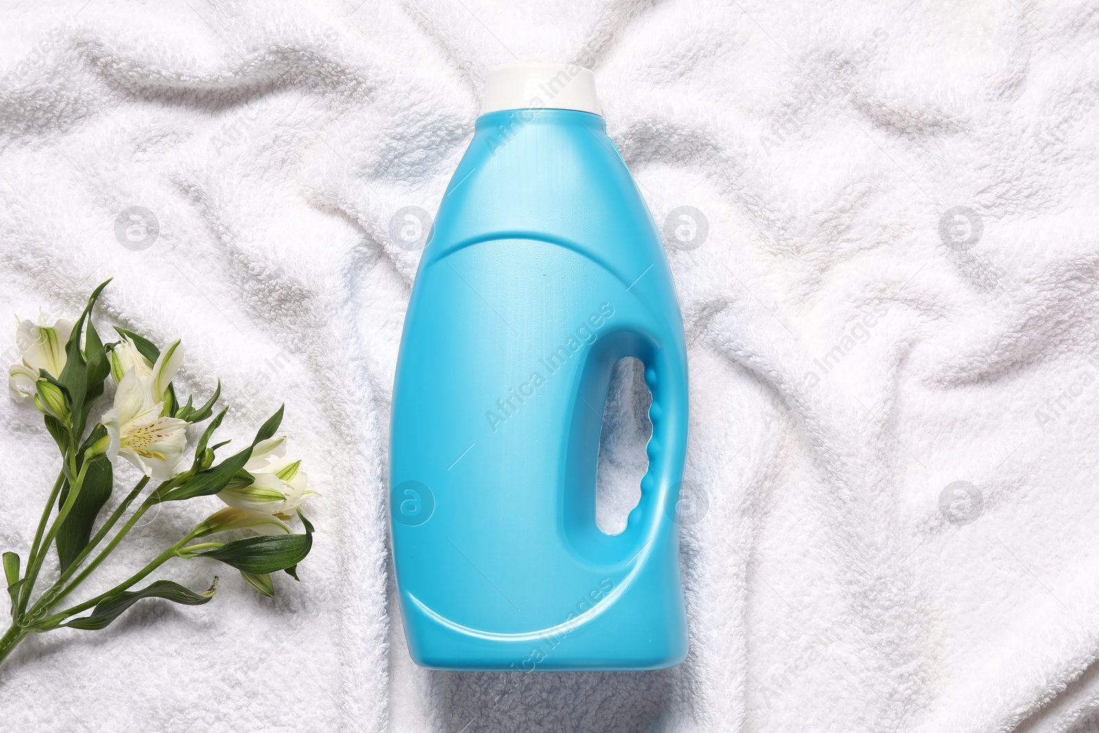 Bottle of fabric softener and flowers on terry towel, flat lay Photo of Bottle of fabric softener and flowers on terry towel, flat lay