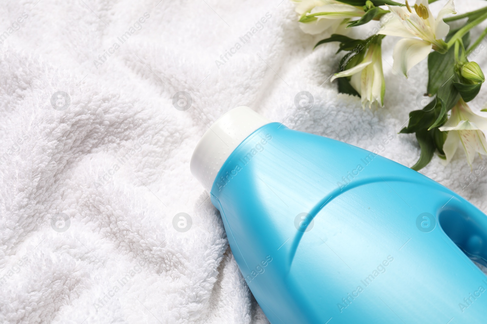 Bottle of fabric softener and flowers on terry towel, above view. Space for text Photo of Bottle of fabric softener and flowers on terry towel, above view. Space for text