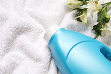 Photo of Bottle of fabric softener and flowers on terry towel, above view. Space for text
