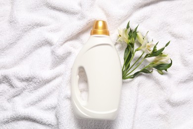 Photo of Bottle of fabric softener and flowers on terry towel, flat lay