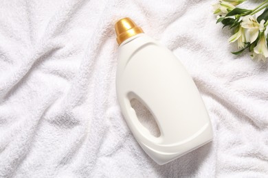 Photo of Bottle of fabric softener and flowers on terry towel, flat lay. Space for text