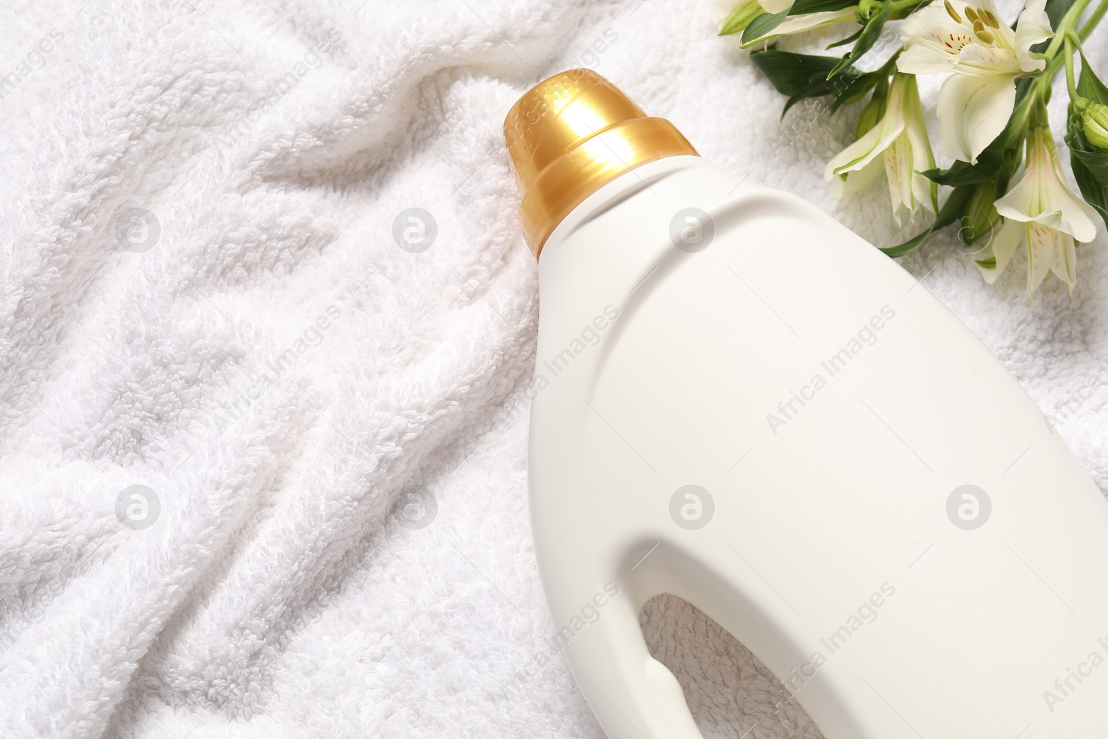 Bottle of fabric softener and flowers on terry towel, flat lay. Space for text Photo of Bottle of fabric softener and flowers on terry towel, flat lay. Space for text