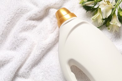 Photo of Bottle of fabric softener and flowers on terry towel, flat lay. Space for text