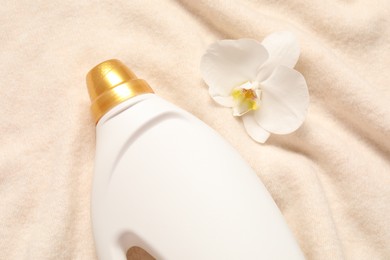 Photo of Bottle of fabric softener and orchid flower on soft cloth, flat lay