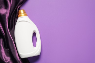 Photo of Bottle of fabric softener and color cloth on purple background, top view. Space for text