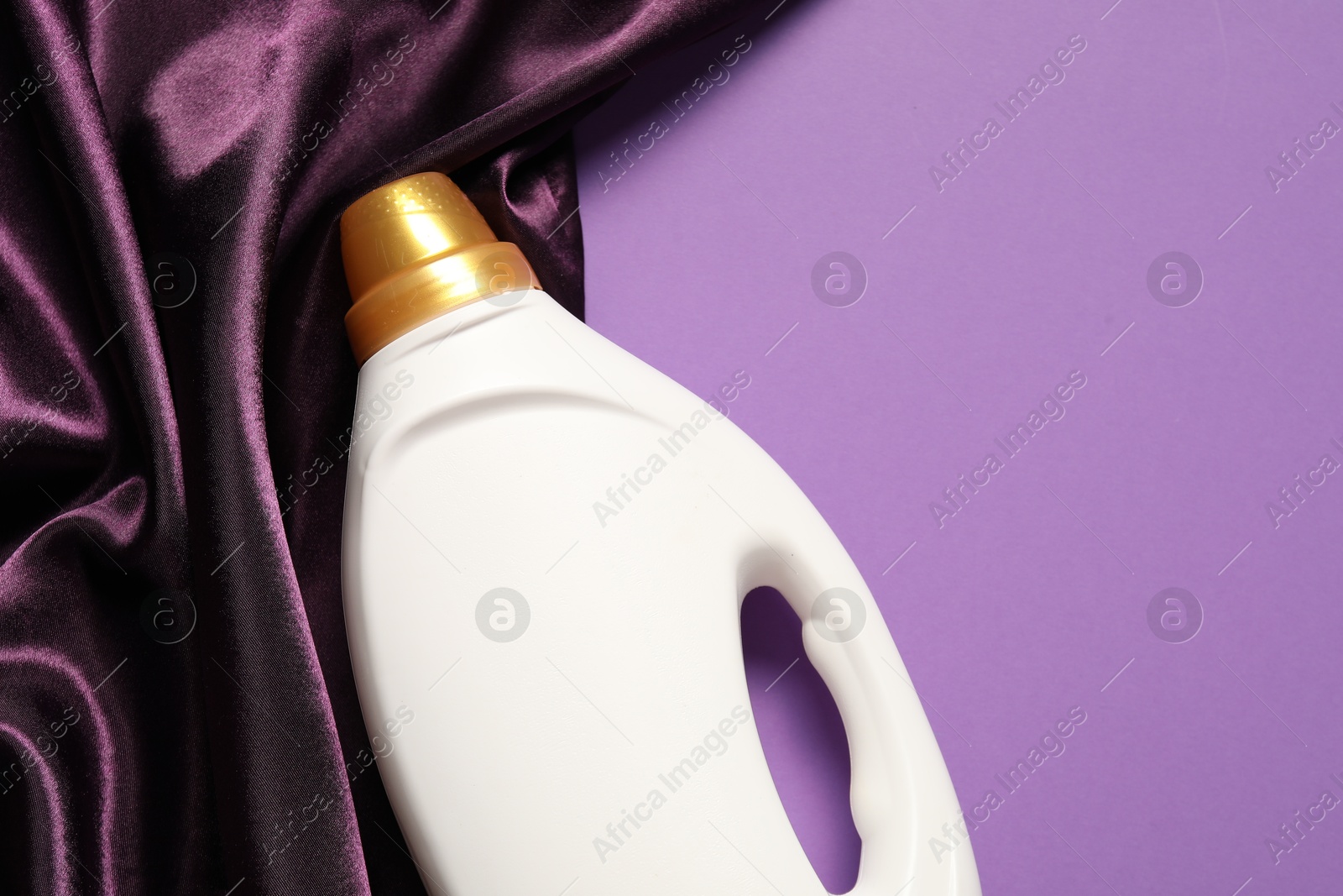 Bottle of fabric softener and color cloth on purple background, top view. Space for text Photo of Bottle of fabric softener and color cloth on purple background, top view. Space for text