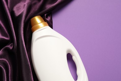 Photo of Bottle of fabric softener and color cloth on purple background, top view. Space for text