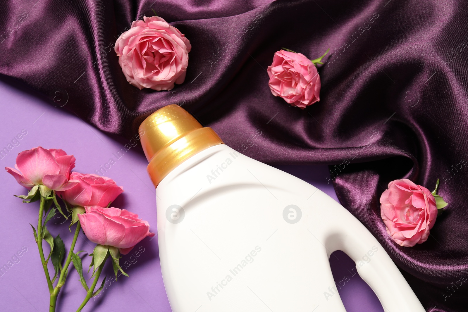 Bottle of fabric softener, flowers and color cloth on purple background, flat lay Photo of Bottle of fabric softener, flowers and color cloth on purple background, flat lay