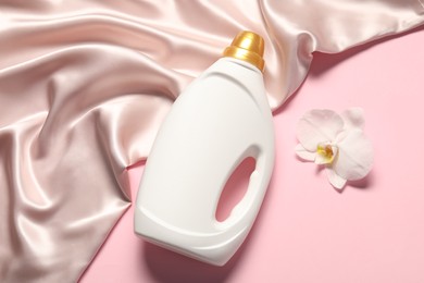Photo of Bottle of fabric softener, orchid flower and beige cloth on pink background, flat lay