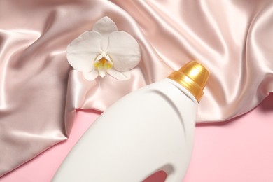 Photo of Bottle of fabric softener, orchid flower and beige cloth on pink background, above view