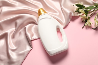Photo of Bottle of fabric softener, flowers and beige cloth on pink background, flat lay